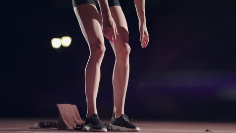 One-woman-in-the-dark-at-the-stadium-is-preparing-to-start-a-race-on-the-track.-Slow-motion-woman-starts-from-hunger-strikes-in-the-stadium-in-the-dark
